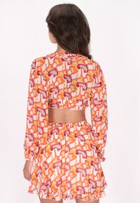 Kleurenset van een cropped blouse en rok in doorzichtig materiaal, met een gedurfde abstracte print in oranje en roze. Volants aan de onderkant en ballonmouwen.
