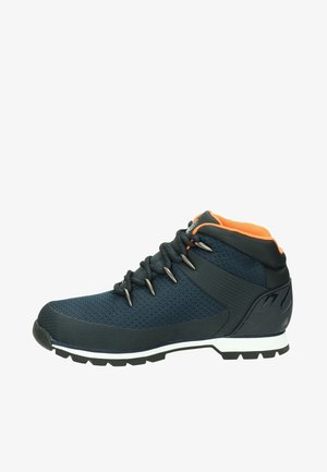Chaussure de randonnée en mesh et matériau synthétique bleu foncé. Présente des accents orange, des œillets en métal et une semelle noire robuste pour l'adhérence.