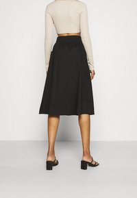 Falda midi negra con diseño acampanado, que presenta un frente plano y una cinturilla elástica, combinada con una blusa ajustada de manga larga.