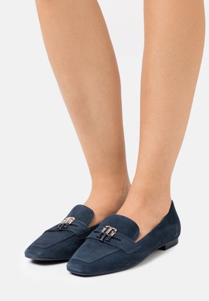 Marineblauwe suède instappers met een spitse neus, decoratieve band en gespdetail, en een lage platte hak. Glad textuur over de gehele schoen.