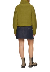 GeCropte olijfgroene trui met een geribbelde kraag, gecombineerd met een donkerdenim mini-jurk. Draagt het met enkelhoge bruine laarzen.