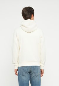 Hvid hoodie med en blød tekstur og en stor hætte, parret med blå jeans. Pasformen er afslappet, og designet er minimalistisk.