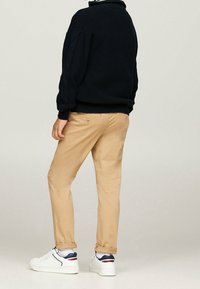 Pull en maille bleu marine, chinos kaki et baskets blanches avec des accents bleu marine et rouge. Les chinos présentent deux boutons à l'arrière et une coupe slim.