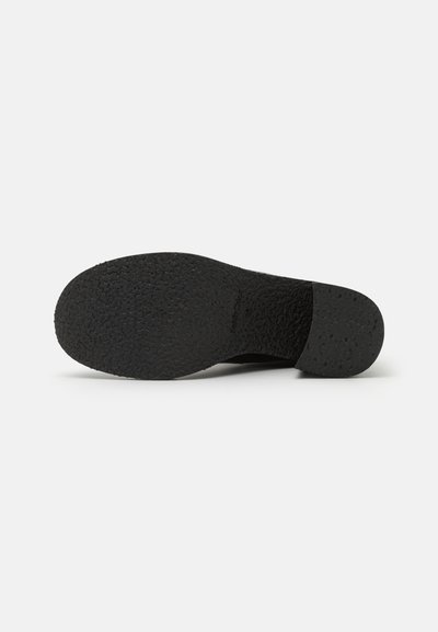 Suela de zapato negra con superficie texturizada, punta redondeada y tacón ligeramente elevado. Diseño minimalista sin marcas o adornos visibles.