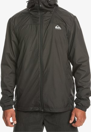 Czarna kurtka wiatrówka na zamek błyskawiczny z kapturem i logo Quiksilver na lewej piersi, noszona przez osobę z rękami swobodnie opuszczonymi wzdłuż ciała.