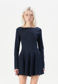 Donkerblauwe long sleeve jurk met een aansluitend lijfje en een uitlopende rok. Gemaakt van denim met zichtbare stikseldetails. Klassieke boot halslijn.