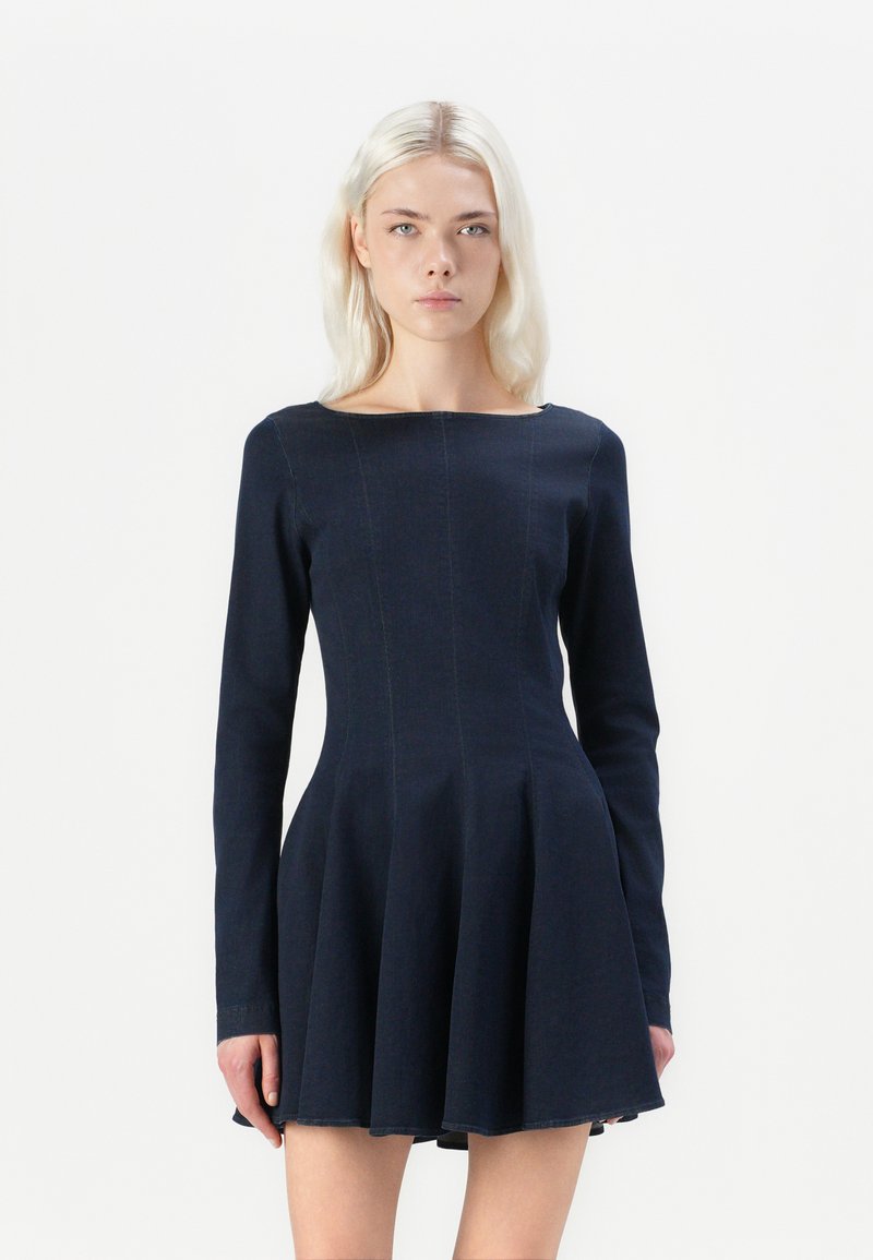 Donkerblauwe long sleeve jurk met een aansluitend lijfje en een uitlopende rok. Gemaakt van denim met zichtbare stikseldetails. Klassieke boot halslijn.
