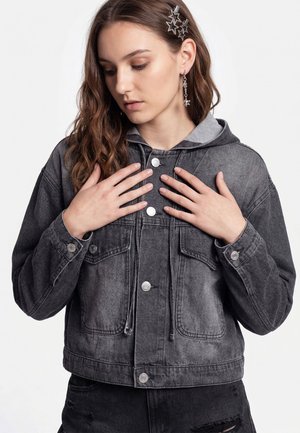 Young woman with long hair wearing a faded black denim jacket, star hair clips, and star-shaped dangling earrings, hands near collar.