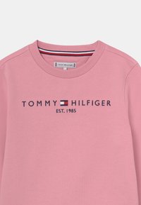 Felpa rosa con collo a giro, polsini a coste e logo ricamato con accenti in rosso, bianco e blu. Il materiale appare morbido e liscio.