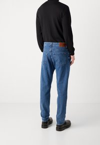 Blå denimjeans med avslappnad passform, med en brun läderlapp vid midjan och två bakfickor. Bärs med en svart långärmad topp.