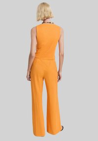 Oranje mouwloze jumpsuit met een aansluitende top en wijde broekspijpen, gemaakt van een textuurstof. Achteraanzicht toont een schoon, minimalistisch ontwerp.