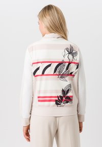 Lichtgewicht beige jack met een gestreepte achterkant met een rood en zwart bloemmotief. Soepele textuur met een aansluitend ontwerp en lange mouwen.