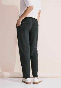 Czarne, lekkie spodnie z elastycznym paskiem, bocznymi kieszeniami i luźnym krojem, zestawione z białymi sneakersami i topem z krótkim rękawem.