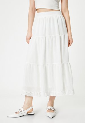 Falda maxi blanca de volante con una tela texturizada, con un dobladillo con volantes. Combinada con zapatos blancos de punta y un top corto.