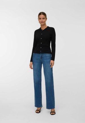 Crna dugosleeve cardigan s ovratnikom, prednjim gumbima i dva mala džepa, uparen s plavim farmerkama ravnog kroja s visokim strukom.