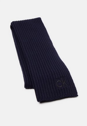 Ciemnogranatowy prążkowany szalik dzianinowy, złożony, z małym czarnym haftowanym logo "ck" w pobliżu krawędzi na białym tle.