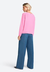 Pink long-sleeve top with a round neckline and back button detail, paired with wide-leg blue denim pants, displayed from a rear angle.