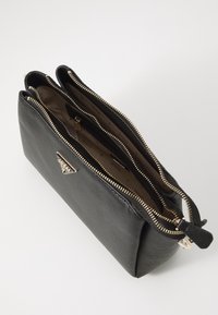 Černá texturovaná kožená peněženka s dvěma otevřenými zipovými přihrádkami a béžovou látkovou podšívkou potištěnou názvem značky.