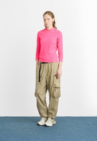 Feszes, hosszú ujjú rózsaszín felső, kerek nyakkal, lazán illeszkedő bézs cargo nadrággal, ami oldalsó zsebekkel rendelkezik, fehér sportcipővel párosítva.