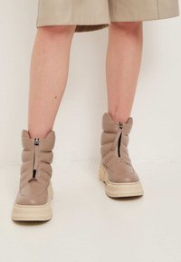 Botas de tobillo tipo puffer en beis con cierre de cremallera, parte superior texturizada y suela de plataforma gruesa que presenta una entresuela de color claro en contraste.