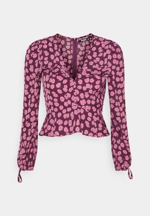 Langærmet lilla bluse med pink blomsterprint, V-hals, flæsedetalje på brystet, peplum-talje og bindebånd på manchetterne.