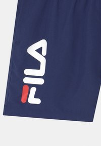 Calções atleticos azul marinho feitos de um tecido leve, com um grande logotipo branco da Fila e um acento vermelho na bainha.