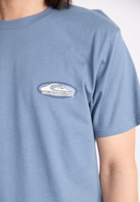 Blå bomulls t-skjorte med et rundbrodert Quiksilver-logo på brystet. Kortermet og med rund hals. Glatt tekstur.