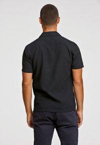 Μαύρο κοντομάνικο πουκάμισο με γιακά, υφαντό ύφασμα και ίσια τελείωμα, απεικονιζόμενο από πίσω.