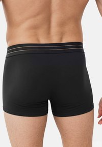 Czarne bokserki o dopasowanym kroju, z gładką teksturą i szerokim pasem w talii ozdobionym dwoma złotymi paskami.