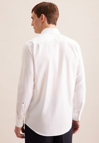 Camicia bianca a maniche lunghe realizzata in tessuto leggero e morbido, con colletto classico, orlo arrotondato e polsini abbottonati.