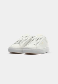 Hvite sneakers med en glatt skinnoverdel, rund tå og gummisåle. Har flate lisser og subtil merking i gull på tungen.