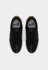 Ζευγάρι μαύρα δερμάτινα αθλητικά παπούτσια με λευκές σόλες και χρυσές λεπτομέρειες, με το λογότυπο "LOVE MOSCHINO" στις εσωτερικές σόλες, φωτογραφημένα από πάνω σε λευκό φόντο.