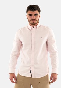 Chemise à rayures rose clair avec des boutons, fabriquée en coton, dotée d'un col pointu, avec un petit logo sur la poitrine gauche et des boutons blancs.
