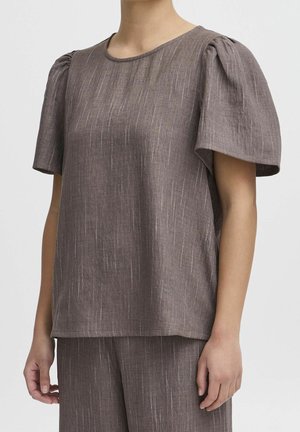 Woman wearing a brown textured short-sleeve top with puffed shoulders and matching pants against a plain background.