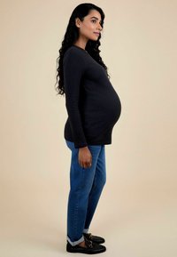 Fekete, hosszú ujjú felső, a melleknél testhez simuló, bordázott textúrával. Kék, egyenes szárú farmer, a bokánál felhajtva. Fekete lakkcipők fém részletekkel.