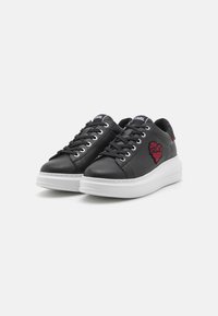 Sneakers in pelle nera con suola bianca, caratterizzati da un design a forma di cuore rosso sul lato e lacci neri. Finitura liscia con punta arrotondata.