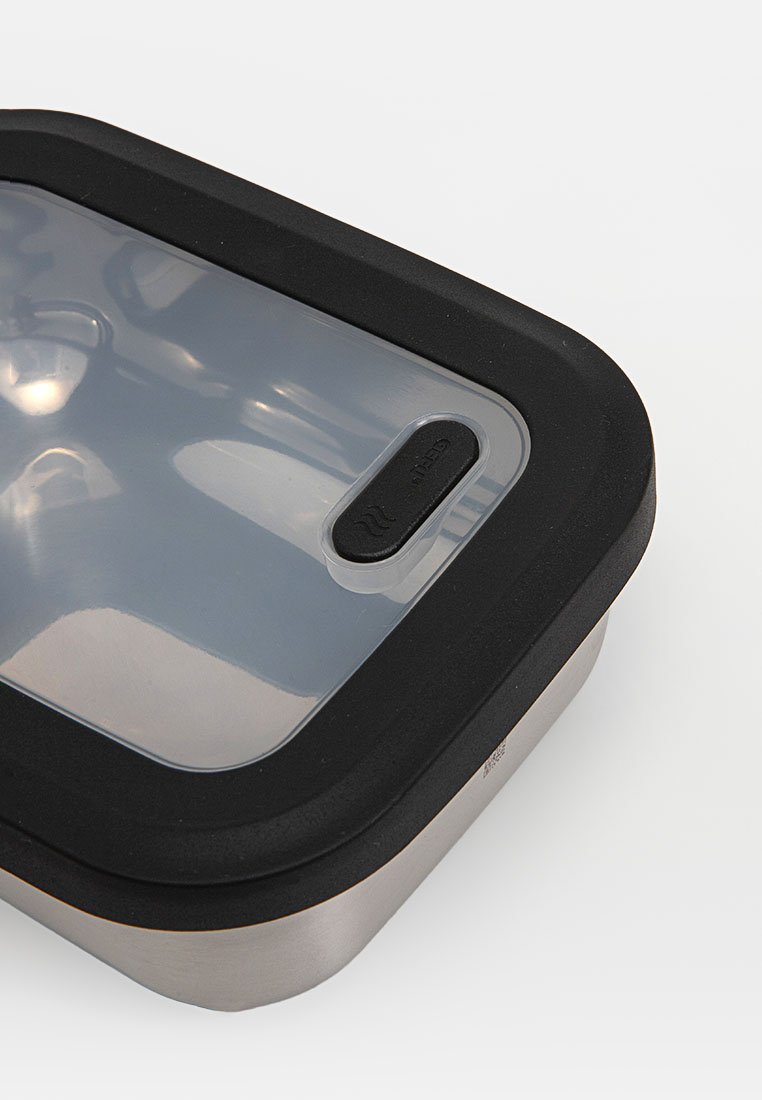Stainless steel food container with a clear, flat lid and black silicone seal. Features a small vent for steam release. Rectangular shape.