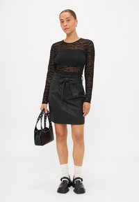 Μαύρη μπλούζα με μακριά μανίκια και διαφανές υφασμάτινο σχέδιο, συνδυασμένη με ψηλόμεση δερμάτινη μίνι φούστα με φιόγκο. Η εμφάνιση ολοκληρώνεται με μαύρη τσάντα και παπούτσια.