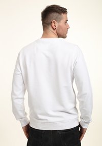 Bílý svetr s dlouhými rukávy, kulatým výstřihem a žebrovanými manžetami. Hladká textura, minimalistický design a žádné viditelné vzory nebo akcenty.