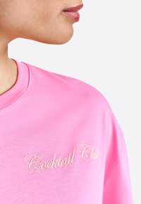Sudadera din bumbac roz, cu "Cocktail Club" brodată cu un fir auriu, în stil cursiv. Textură netedă și design clasic cu guler rotund.