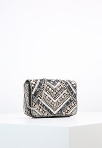 Borsa a mano in perline di colore nero, argento e beige. Presenta un motivo a zigzag, una tracolla a catena e decorazioni decorative sulla superficie.