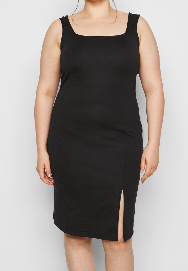Femme portant une robe noire sans manches jusqu'au genou, avec un décolleté carré et une fente frontale du côté droit.