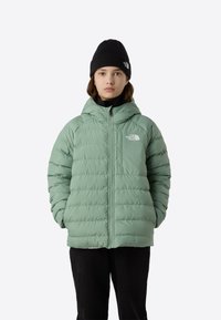 Heleroheline kapuutsi ja horisontaalse tikkimisega puffer-jope, esikinniseks tõmblukk ja väike logo rinnal. Komplektis musta värvi müts.