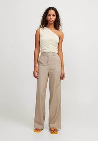 Beežid linased laia lõikega püksid, mis on kombineeritud keharõhuga ühes õlas kreemja toppiga. Jalanõudeks on kollased madala kontsaga sandaalid lihtsa disainiga.