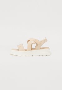 Sandale beige avec des brides croisées et un bout carr�é. Présente une semelle compensée blanche texturée et un dessus lisse. Pas de quincaillerie visible.