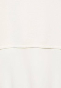 Off-white topp med en texturerad stickad design. Har en slät nederkant och subtil sömdetalj över bröstområdet.