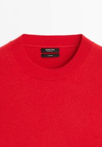 Pull en cachemire rouge vif à col rond côtelé, étiqueté "Massimo Dutti Made in China" à l'intérieur de l'encolure.