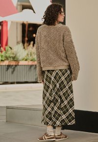 Beiger, flauschig-texturierter Pullover mit geripptem Saum, kombiniert mit einem karierten, knielangen Rock in Grün und Weiß. Braune Sneaker mit hellgrauen Socken.