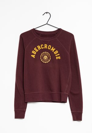 Bordowa krótka bluza z żółtym napisem "Abercrombie" i okrągłym logo, zawieszona na czarnym wieszaku na białym tle.