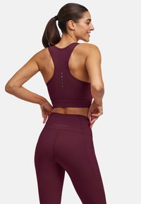 Maroonowy sportowy crop top z szerokimi ramiączkami, gładką teksturą i designem racerback. W połączeniu z leggingsami o wysokim stanie z kropkowymi akcentami.